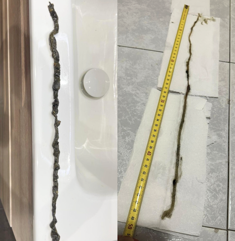 Cadena alargada y de apariencia rústica colocada sobre una bañera blanca a la izquierda y sobre un piso de baldosas grises a la derecha, con una cinta métrica que mide aproximadamente 50 centímetros.